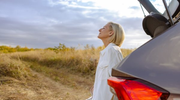 Side view of blond-haired woman standing next to the car and enjoying the view