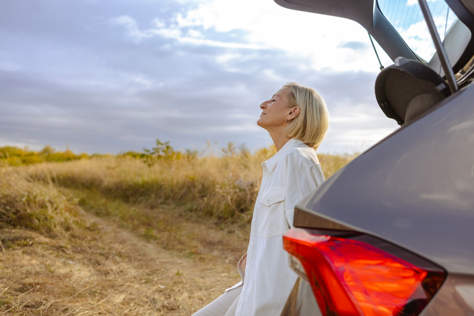 Side view of blond-haired woman standing next to the car and enjoying the view