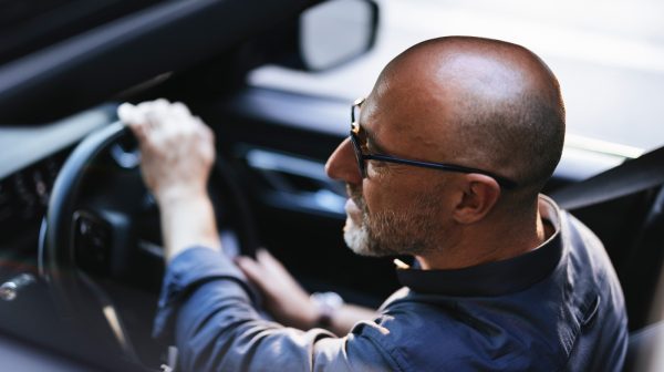 A businessman is seen driving a car through a sunny urban city. The image conveys a sense of independence and focus while navigating the bustling streets.